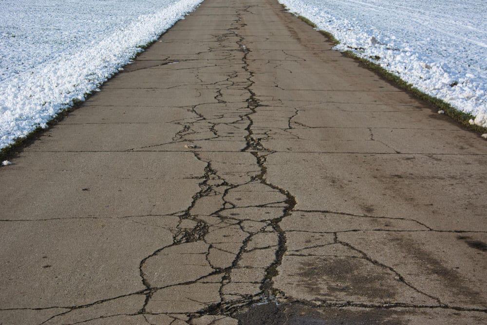 Close-up of ice sitting inside a crack in an unsealed asphalt driveway during winter.